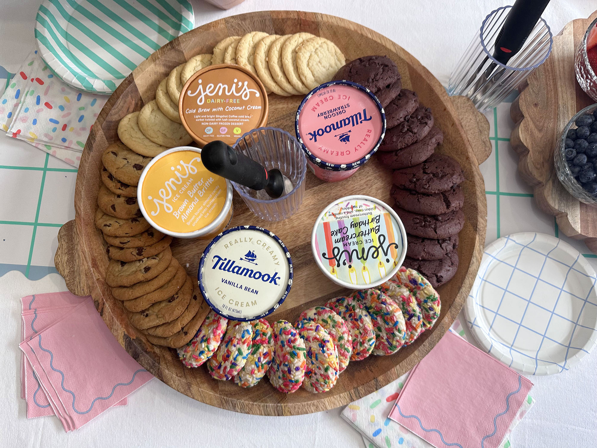 Multiple different flavor cookies surrounding pints of Jeni's Ice cream flavors and Tillamook ice cream flavors on a large tray. striped plates and different fun napkin designs