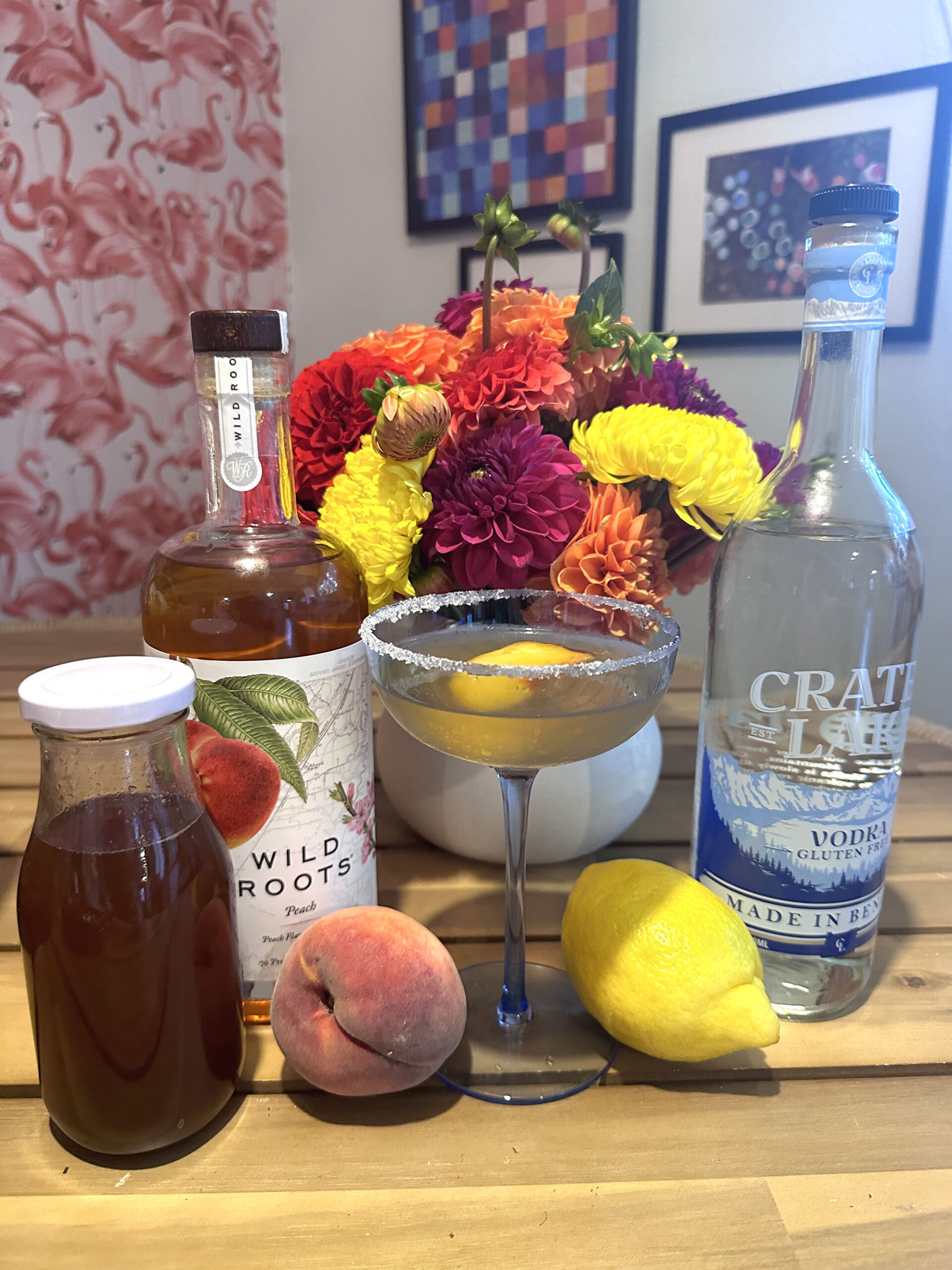 Cocktail with peach and lemon, crater lake vodka, wild roots peach vodka, spiced peach simple syrup, and brightly colored mums